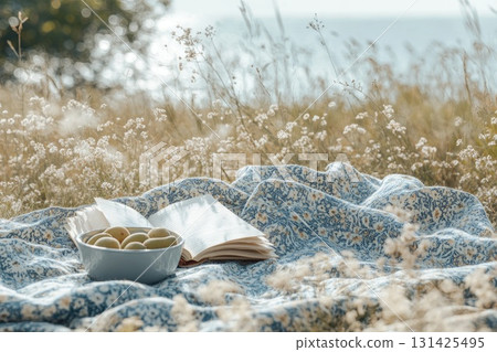 Cozy picnic scene with open book and bowl of fruits on floral blanket in serene nature 131425495