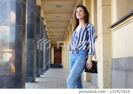 Beautiful smiling girl in trendy casual clothes. Outdoor street style portrait with print shirt, jeans and handbag. Modern lifestyle, fashion model concept Beautiful smiling girl in trendy casual clothes. Outdoor street style portrait with print shirt, jeans and handbag. Modern lifestyle, fashion model concept 131425828