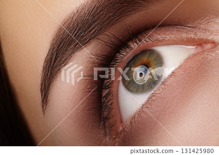 Macro closeup of green female eye with soft brown smoky makeup and thick natural brow enhanced by permanent tattoo. Concept for professional makeup, vision and eye health Macro closeup of green female eye with soft brown smoky makeup and thick natural brow enhanced by permanent tattoo. Concept for professional makeup, vision and eye health 131425980