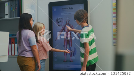 Two Girls and Boy Interact With Large Digital Screen Displaying 3D Model of Human Body in Classroom Two Girls and Boy Interact With Large Digital Screen Displaying 3D Model of Human Body in Classroom 131425982