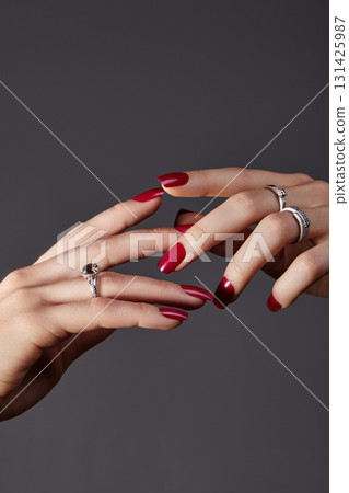 Close up of female hands with perfect red manicure on nails and elegant jewelry. Shiny polished nails, timeless classic nail art, luxury rings in gold and platinum with sparkling diamonds Close up of female hands with perfect red manicure on nails and elegant jewelry. Shiny polished nails, timeless classic nail art, luxury rings in gold and platinum with sparkling diamonds 131425987