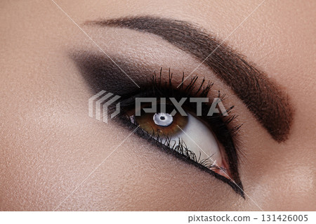 Closeup macro of female eye with bold dark smoky makeup and dramatic eyeliner. Editorial fashion look for runway, Halloween party, gothic style and mysterious vampire aesthetic Closeup macro of female eye with bold dark smoky makeup and dramatic eyeliner. Editorial fashion look for runway, Halloween party, gothic style and mysterious vampire aesthetic 131426005
