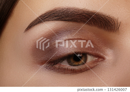 Macro closeup of green eye with brown smoky makeup, thick brow with permanent tattoo and mascara on natural lashes. Perfect for beauty, fashion and medical vision concepts 131426007