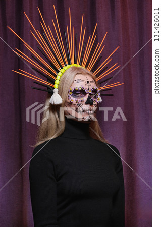Blonde woman with sugar skull makeup and large orange crown shaped like sun rays. Unique ceremonial look reflecting cultural heritage, beauty, creativity and tradition Blonde woman with sugar skull makeup and large orange crown shaped like sun rays. Unique ceremonial look reflecting cultural heritage, beauty, creativity and tradition 131426011