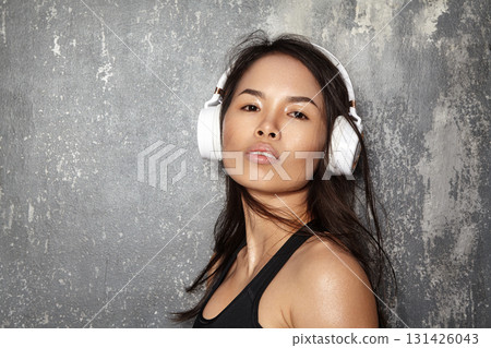 Portrait of young Asian woman wearing wireless white headphones, hair moving in motion as she listens to music. Modern lifestyle, sound, technology and youth culture theme Portrait of young Asian woman wearing wireless white headphones, hair moving in motion as she listens to music. Modern lifestyle, sound, technology and youth culture theme 131426043