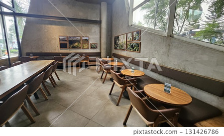 This spacious and modern cafe features smooth concrete walls and tiled flooring, creating an industrial-chic atmosphere where warm wooden tables and comfortable leather chairs are arranged along long This spacious and modern cafe features smooth concrete walls and tiled flooring, creating an industrial-chic atmosphere where warm wooden tables and comfortable leather chairs are arranged along long 131426786