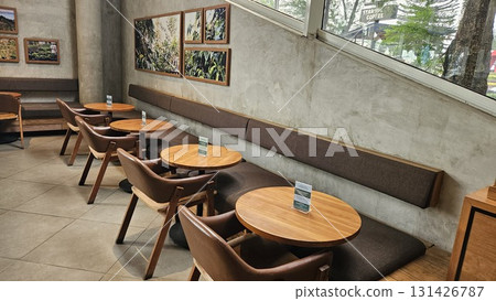 This spacious and modern cafe features smooth concrete walls and tiled flooring, creating an industrial-chic atmosphere where warm wooden tables and comfortable leather chairs are arranged along long This spacious and modern cafe features smooth concrete walls and tiled flooring, creating an industrial-chic atmosphere where warm wooden tables and comfortable leather chairs are arranged along long 131426787