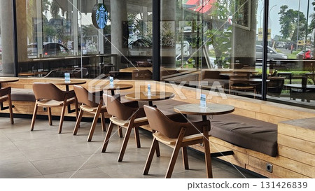 This spacious and modern cafe features smooth concrete walls and tiled flooring, creating an industrial-chic atmosphere where warm wooden tables and comfortable leather chairs are arranged along long, This spacious and modern cafe features smooth concrete walls and tiled flooring, creating an industrial-chic atmosphere where warm wooden tables and comfortable leather chairs are arranged along long, 131426839