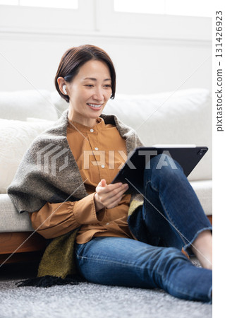 A middle-aged woman using a tablet with wireless earphones A middle-aged woman using a tablet with wireless earphones 131426923