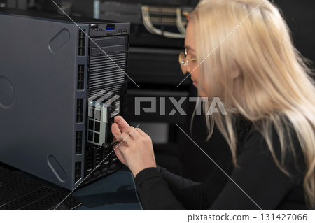 Female IT technician in their 20s working on a server rack in a data center 131427066
