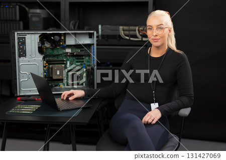 Female IT technician in her 30s with laptop beside open server, performing hardware maintenance and diagnostics 131427069