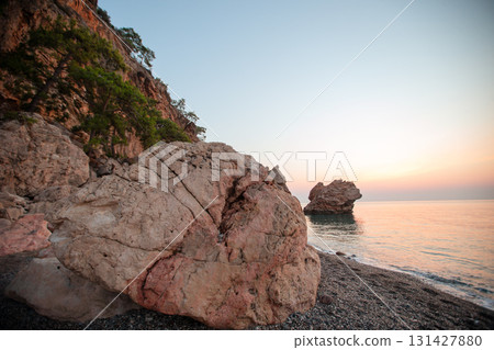 Seascape in the mountains. A large rock on the seashore. The water is calm and the sky is a beautiful orange color. 131427880