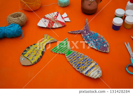 Assemble a fish using cardboard, thread, and paint, with clear instructions, against an orange background. Assemble a fish using cardboard, thread, and paint, with clear instructions, against an orange background. 131428284