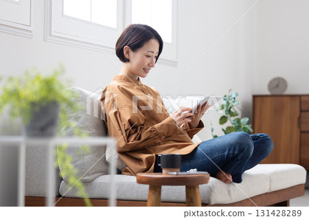 Middle-aged woman operating a tablet on the sofa Middle-aged woman operating a tablet on the sofa 131428289