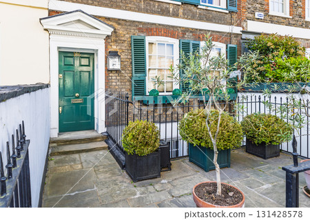 Classic London townhouse entrance with green door, brick facade, and potted topiary Classic London townhouse entrance with green door, brick facade, and potted topiary 131428578