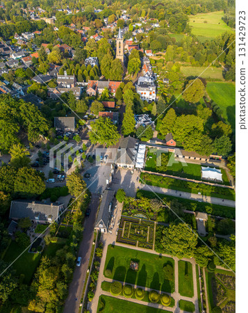 Aerial view of picturesque town with tall steeple church, formal garden, tree lined streets, and historic buildings showcasing harmony between architecture and natural design. 131429723