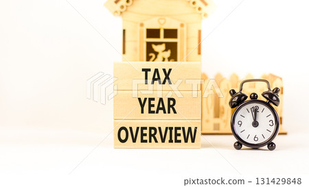 Tax year overview symbol. Concept words Tax year overview on beautiful wooden blocks. Beautiful white background. Black alarm clock. Business tax year overview concept. Copy space. Tax year overview symbol. Concept words Tax year overview on beautiful wooden blocks. Beautiful white background. Black alarm clock. Business tax year overview concept. Copy space. 131429848