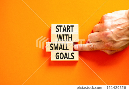 Start with small goals symbol. Concept words phrase Start with small goals on beautiful wooden blocks. Beautiful orange background Businessman's hand Business Start with small goals concept Copy space 131429856