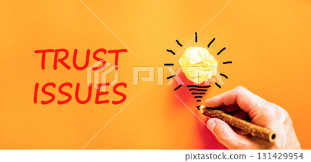 Trust issues symbol. Concept word Trust issues on beautiful orange paper. Businessman's hand. Light bulb icon. Beautiful orange paper background. Business trust issues concept. Copy space. 131429954