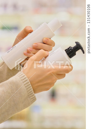 Customer choosing facial cleanser in a cosmetics store. Woman comparing gel, foam or enzyme powder for skincare. Reading ingredients. Close-up hands holding bottles. Concept of conscious beauty choice Customer choosing facial cleanser in a cosmetics store. Woman comparing gel, foam or enzyme powder for skincare. Reading ingredients. Close-up hands holding bottles. Concept of conscious beauty choice 131430106