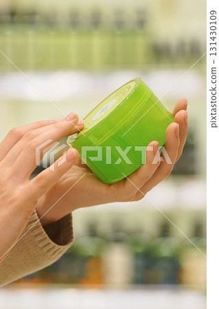 Close up of woman holding a jar in a beauty store, reading label and ingredients. Female shopper examining cosmetic product before purchase. Concept conscious choice for skincare, haircare products. 131430109