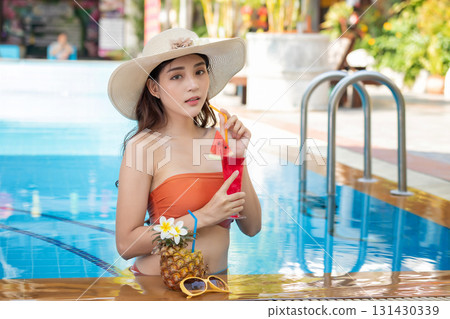 Sexy young asian woman in swimsuits in summer. beautiful woman in orange bikini with hat and tropical drink in swimming pool. 131430339