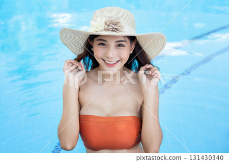 Sexy young asian woman in swimsuits in summer. beautiful woman in orange bikini and hat in swimming pool with tropical drink. 131430340