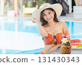Sexy young asian woman in swimsuits in summer. beautiful woman in orange bikini with hat and tropical drink in swimming pool. 131430343