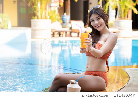 Sexy young asian woman in swimsuits in summer. beautiful woman in orange bikini with sunglasses and tropical drink sitting in swimming pool. 131430347