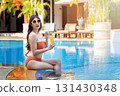 Sexy young asian woman in swimsuits in summer. beautiful woman in orange bikini with sunglasses and tropical drink sitting in swimming pool. 131430348