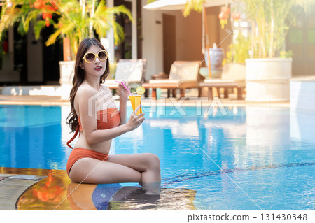 Sexy young asian woman in swimsuits in summer. beautiful woman in orange bikini with sunglasses and tropical drink sitting in swimming pool. 131430348