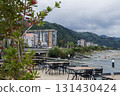 An outdoor dining area with wooden tables and black chairs arranged in rows, overlooking a serene sea with mountains in the background. 131430424