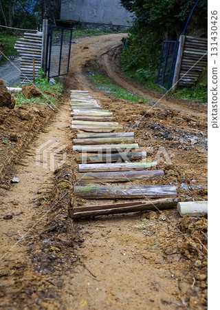The road is unpaved, with a mix of dirt and small wooden planks, and it curves gently to the right.The mood is serene and rustic, evoking a sense of adventure or exploration in a natural setting. 131430426