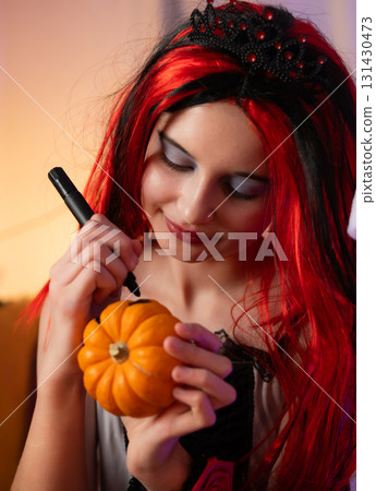 Cute Little Girl In A Halloween Witch Wig Plays With A Pumpkin And Draws A Face For Festive Decorations Cute Little Girl In A Halloween Witch Wig Plays With A Pumpkin And Draws A Face For Festive Decorations 131430473