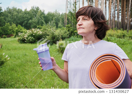 Mature woman with yoga mat and bottle of water in park 131430627
