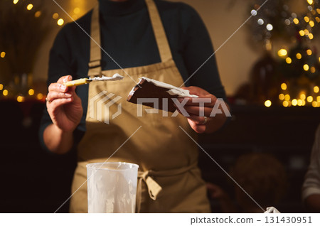 Cozy Christmas Home Kitchen With Apron-Clad Person Frosting Cake For Holiday Baking Cozy Christmas Home Kitchen With Apron-Clad Person Frosting Cake For Holiday Baking 131430951