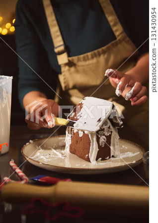 Gingerbread House Being Decorated With White Icing By Hands On A Plate Gingerbread House Being Decorated With White Icing By Hands On A Plate 131430954