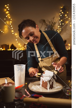 Joyful Home Baker Decorating Gingerbread House For Christmas Celebration In Cozy Kitchen Joyful Home Baker Decorating Gingerbread House For Christmas Celebration In Cozy Kitchen 131430955