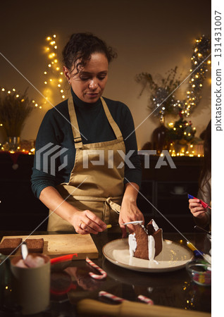 Warm Christmas Kitchen Scene With Mom And Kids Building A Gingerbread House 131431007