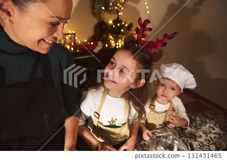 Joyful Mother and Two Kids Baking Christmas Treats Together in a Cozy Home Kitchen 131431465