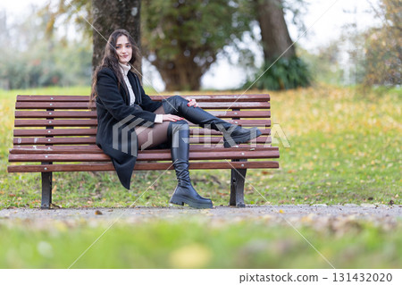 Young woman sitting on a park bench in autumn Young woman sitting on a park bench in autumn 131432020