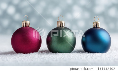 Colorful Christmas ornaments in burgundy, emerald, and royal blue colors resting on soft snow, creating a festive holiday atmosphere with copy space 131432102