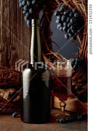 An antique bottle of port wine against the backdrop of an old weathered board, dried vine, and blue grapes. An antique bottle of port wine against the backdrop of an old weathered board, dried vine, and blue grapes. 131432350
