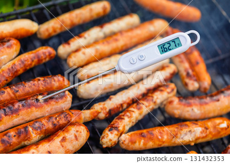 Grilled sausages on barbecue with digital meat thermometer showing safe cooking temperature 131432353