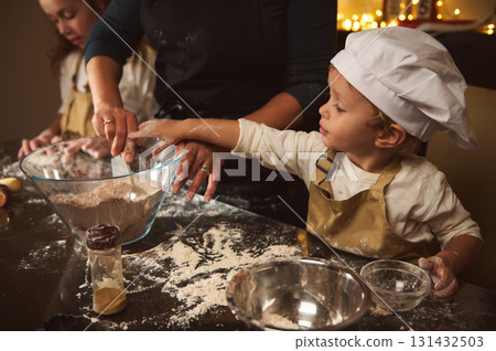 Cute Child Chef Helps Mom Bake Gingerbread House During Cozy Christmas Kitchen Moment 131432503