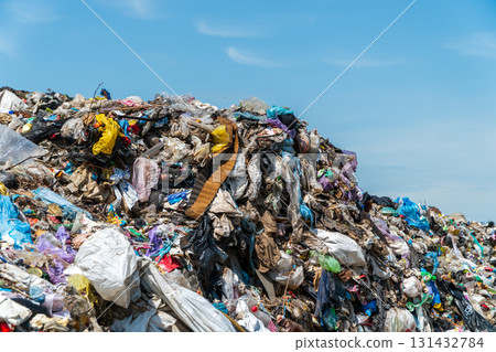 A massive mound of trash filled with plastic, fabric, and other debris is seen against a bright blue sky, highlighting waste management issues 131432784