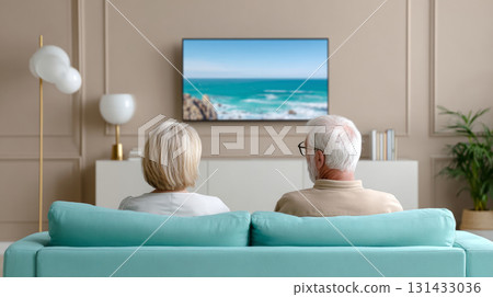 A couple sitting on a couch in a modern living room, watching a nature documentary on a large TV screen with soft lighting that creates a cozy atmosphere. A couple sitting on a couch in a modern living room, watching a nature documentary on a large TV screen with soft lighting that creates a cozy atmosphere. 131433036