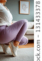 Close-up shot of a plus-size woman in yoga pants and sneakers performing squat exercise at home 131433378