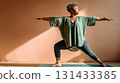 Focused plus-size Black woman practicing warrior yoga pose indoors with sunlight and shadow play 131433385