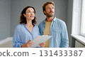 Couple inspecting empty room with clipboard discussing renovation or real estate plans 131433387